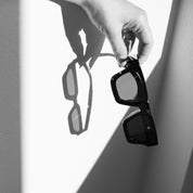 Person holding a pair of sunglasses with a white background
