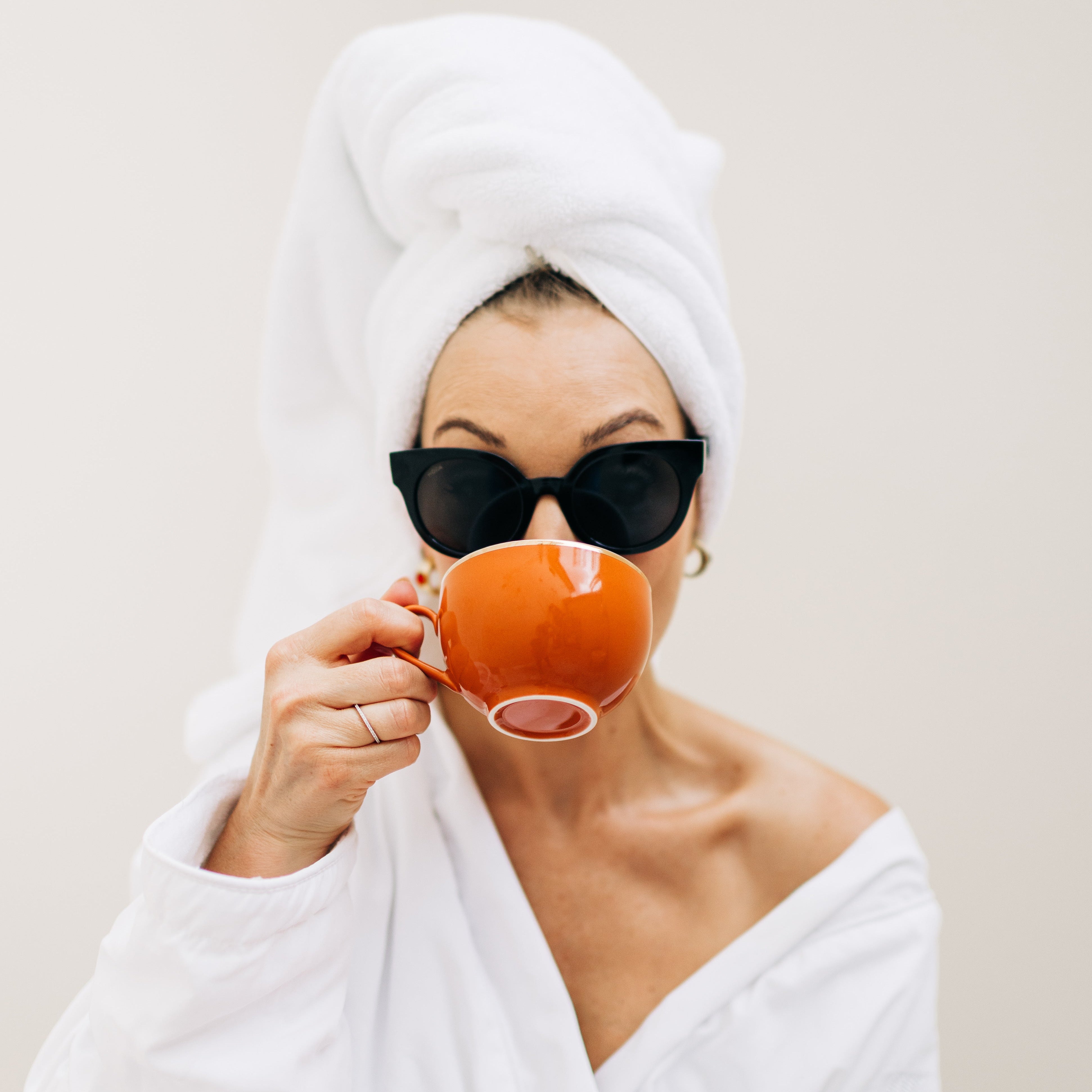 Woman in a white robe and towel wrapped around her head, drinking from an orange cup.